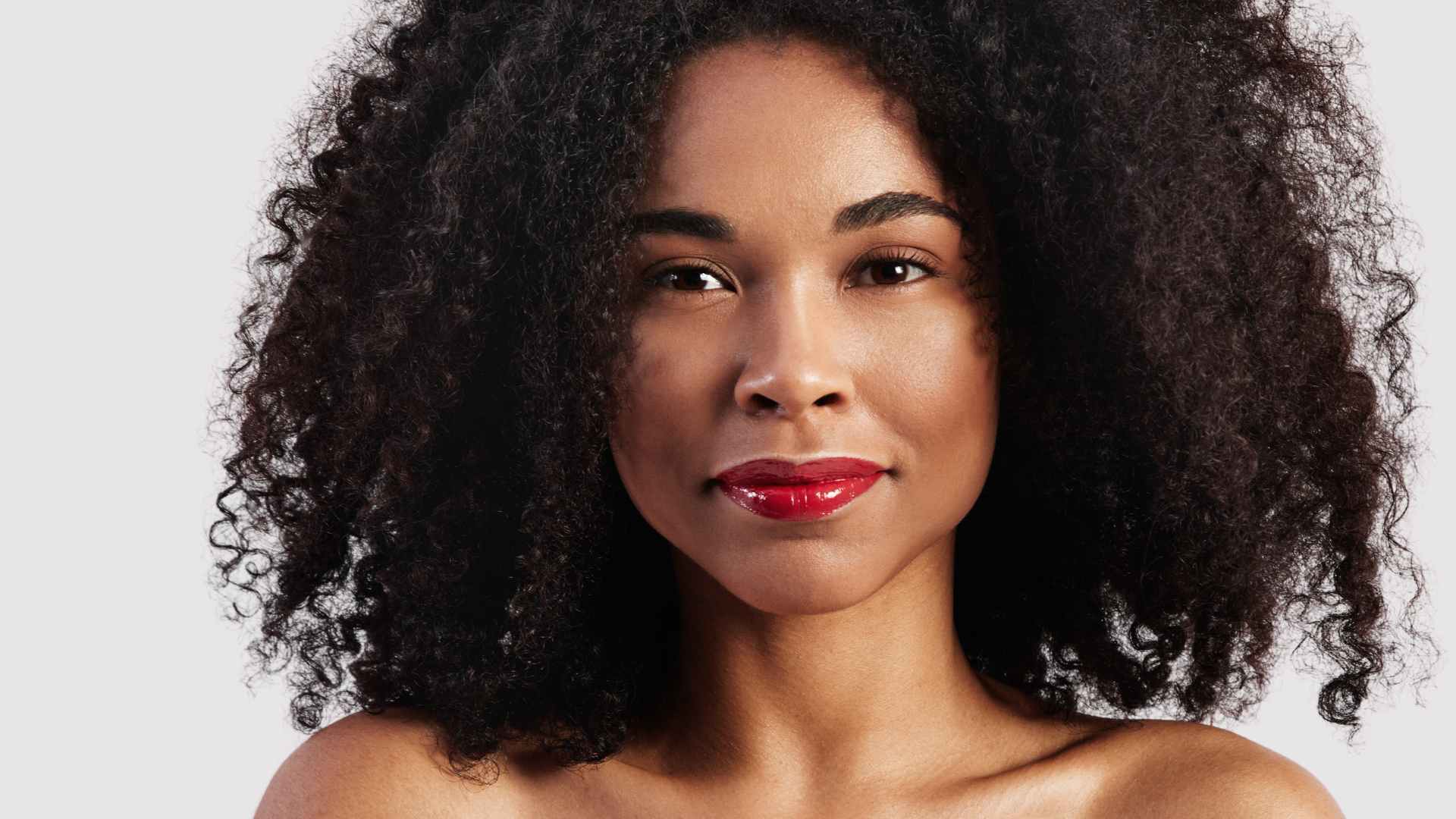 female with red lipstick smiling with shiny black afro hair