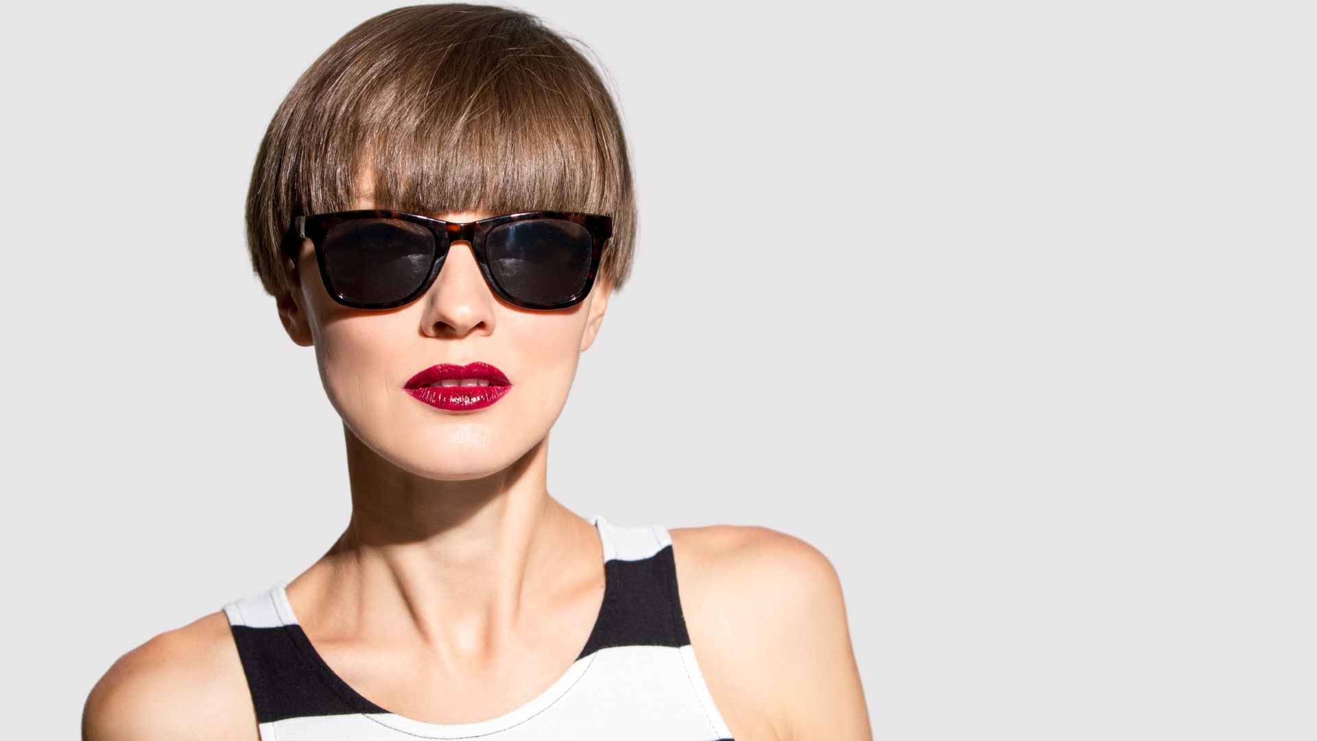 Female model with brown, shiny fine hair. Wearing dark sunglasses, red lipstick and volume in the fringe.