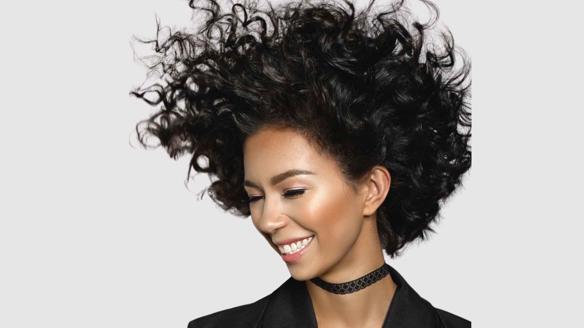 smiling female, eyes closed, black curly hair styled and lifted with sugar spray styling mist
