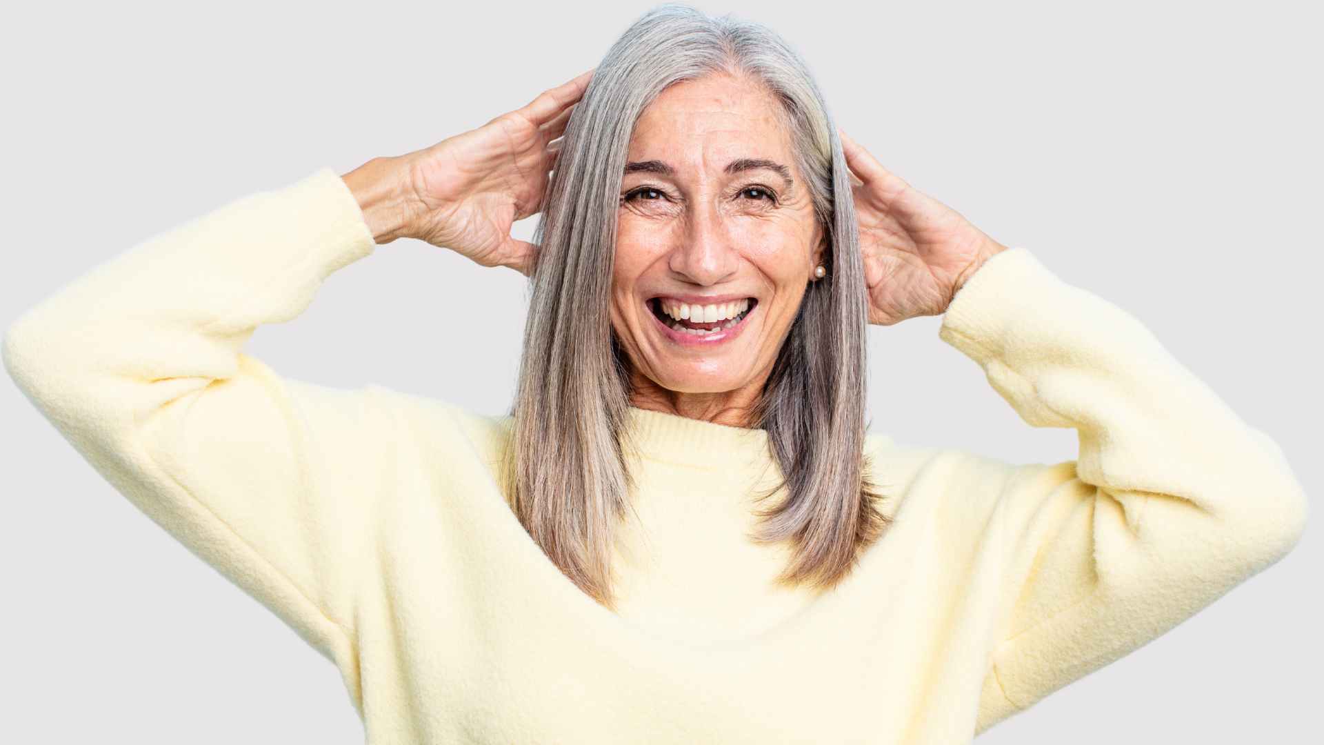 smiling woman with long grey hair, hands to head representing how to look after grey hair