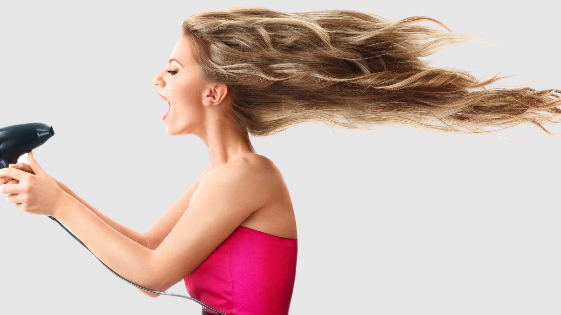 Female with long blonde hair holding a hair dryer to lift her hair